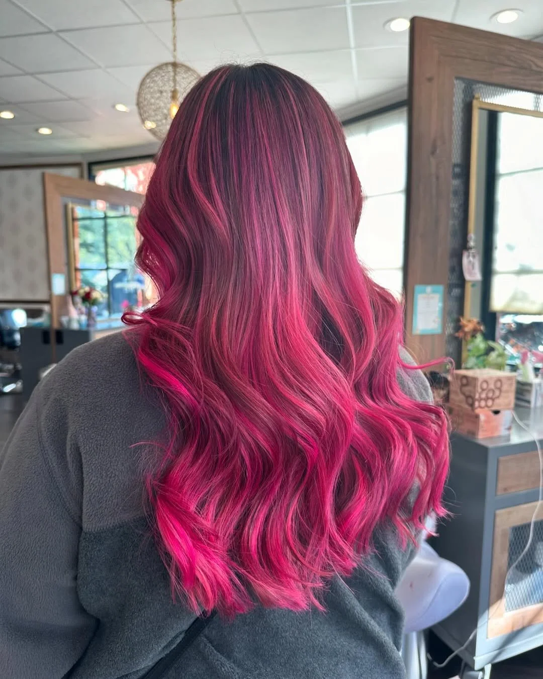 Back view of a person with vibrant pink hair styled in loose waves in a salon setting.