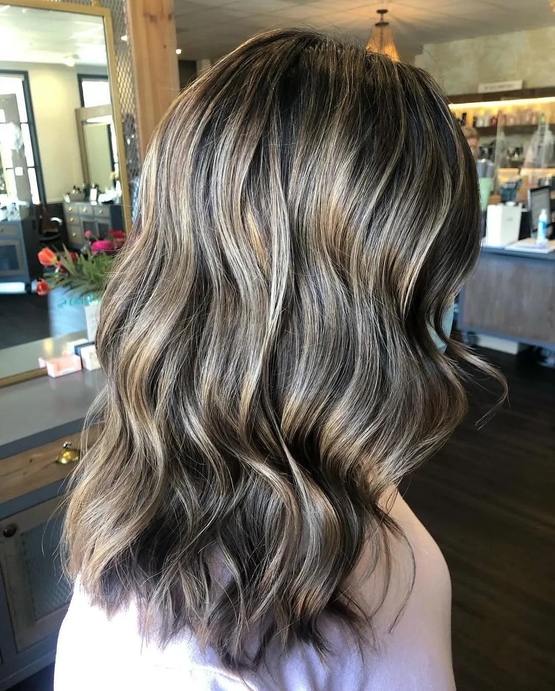 Close-up of a woman's wavy, shoulder-length hair with balayage highlights in shades of blonde, brown, and caramel, styled in loose waves.