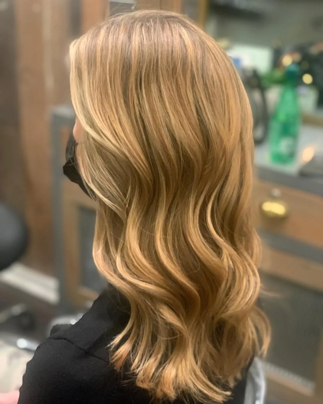 Side view of a woman with wavy, blonde hair styled in loose waves, in a salon setting.