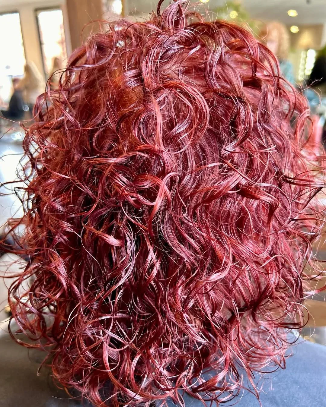 Close-up of a person's curly hair dyed in shades of pink and red.