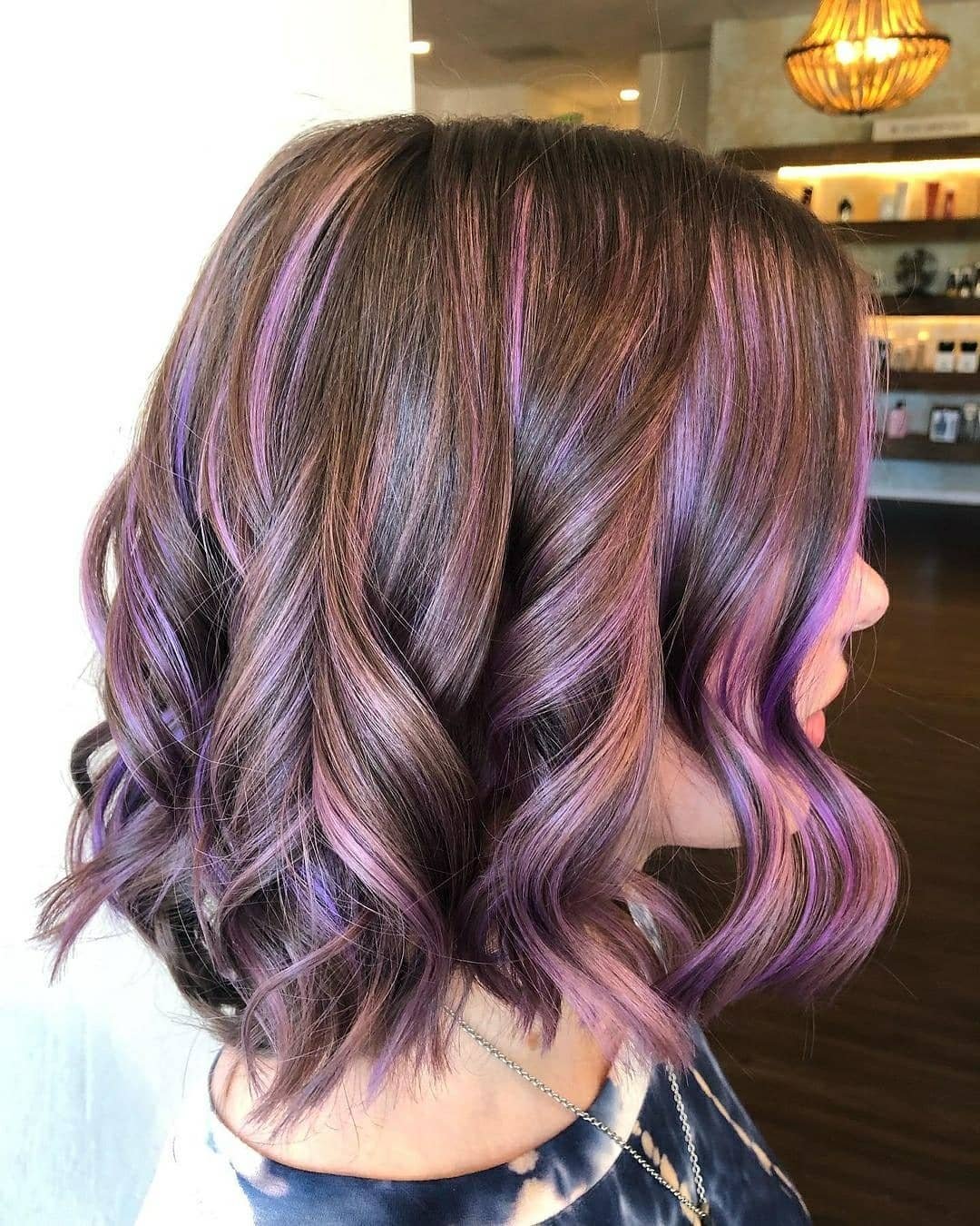 A woman with shoulder-length wavy hair colored with shades of brown, purple, and pink.
