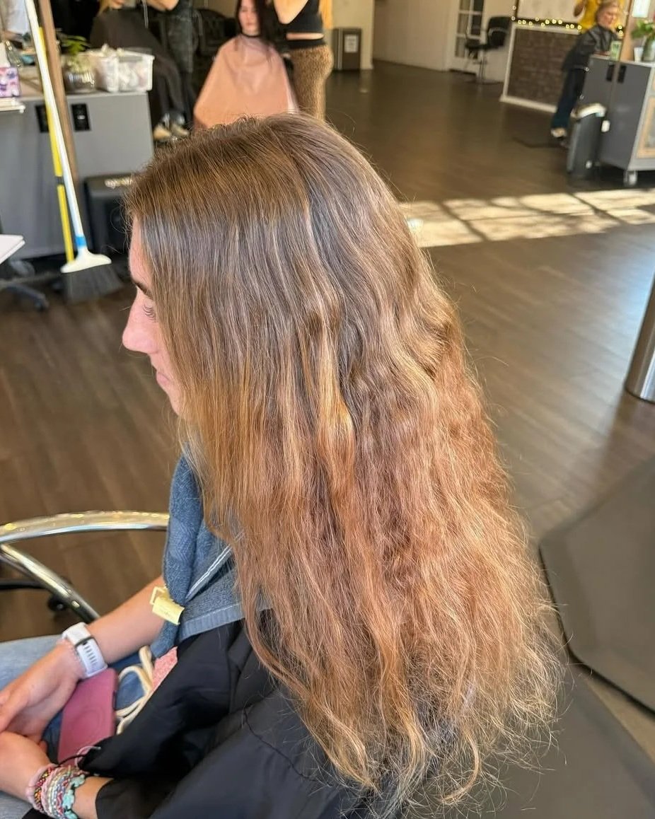 Woman with uneven brown hair, some parts appearing curly and frizzy, sitting in a salon waiting area.