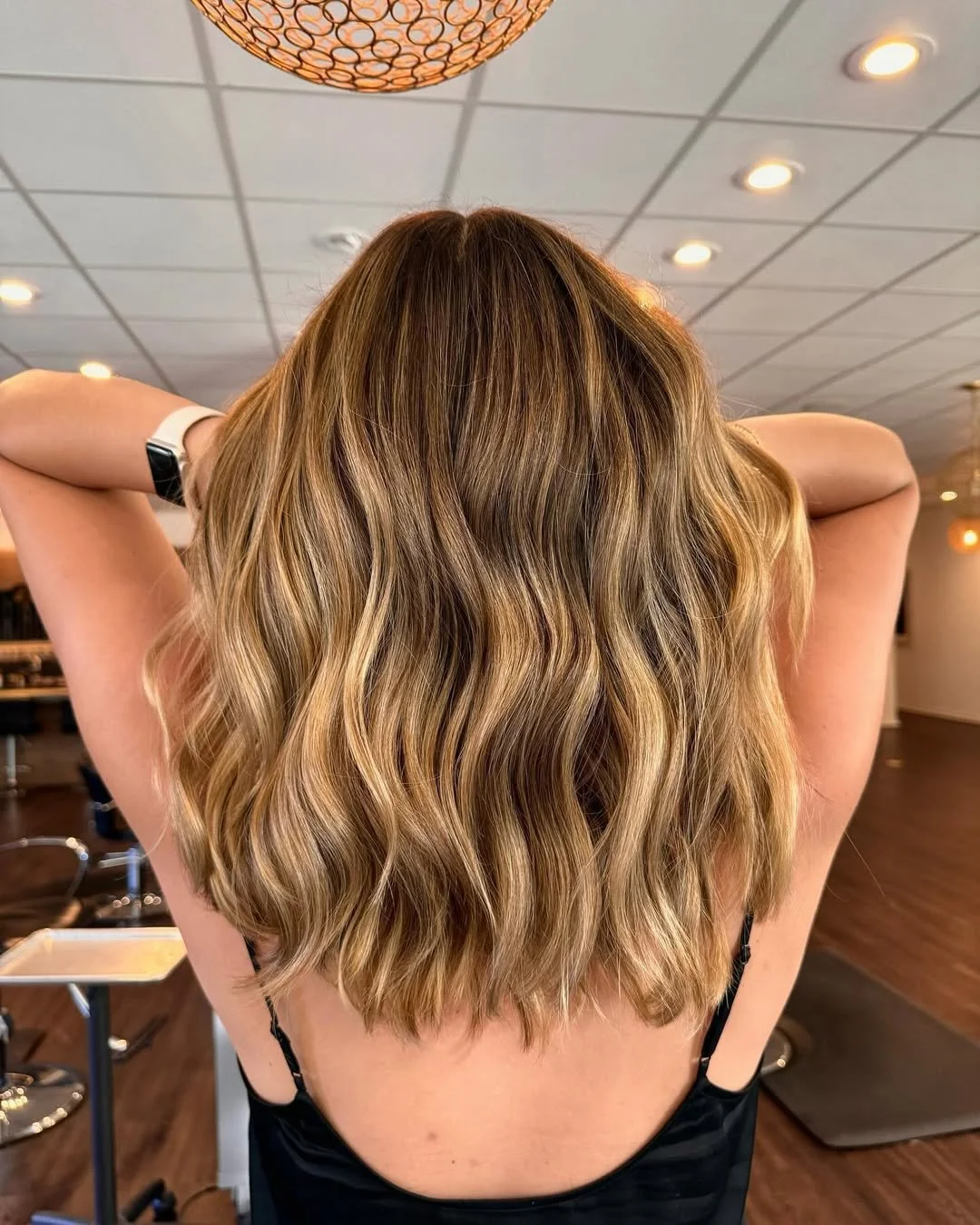 Back view of a woman with shoulder-length, wavy, golden blonde hair in a salon setting.