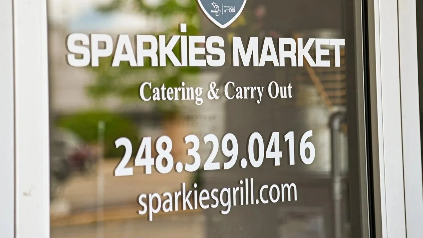Sign on door for Sparkies Market advertising catering and takeout, with phone number 248-329-0416 and website sparkiesgrill.com