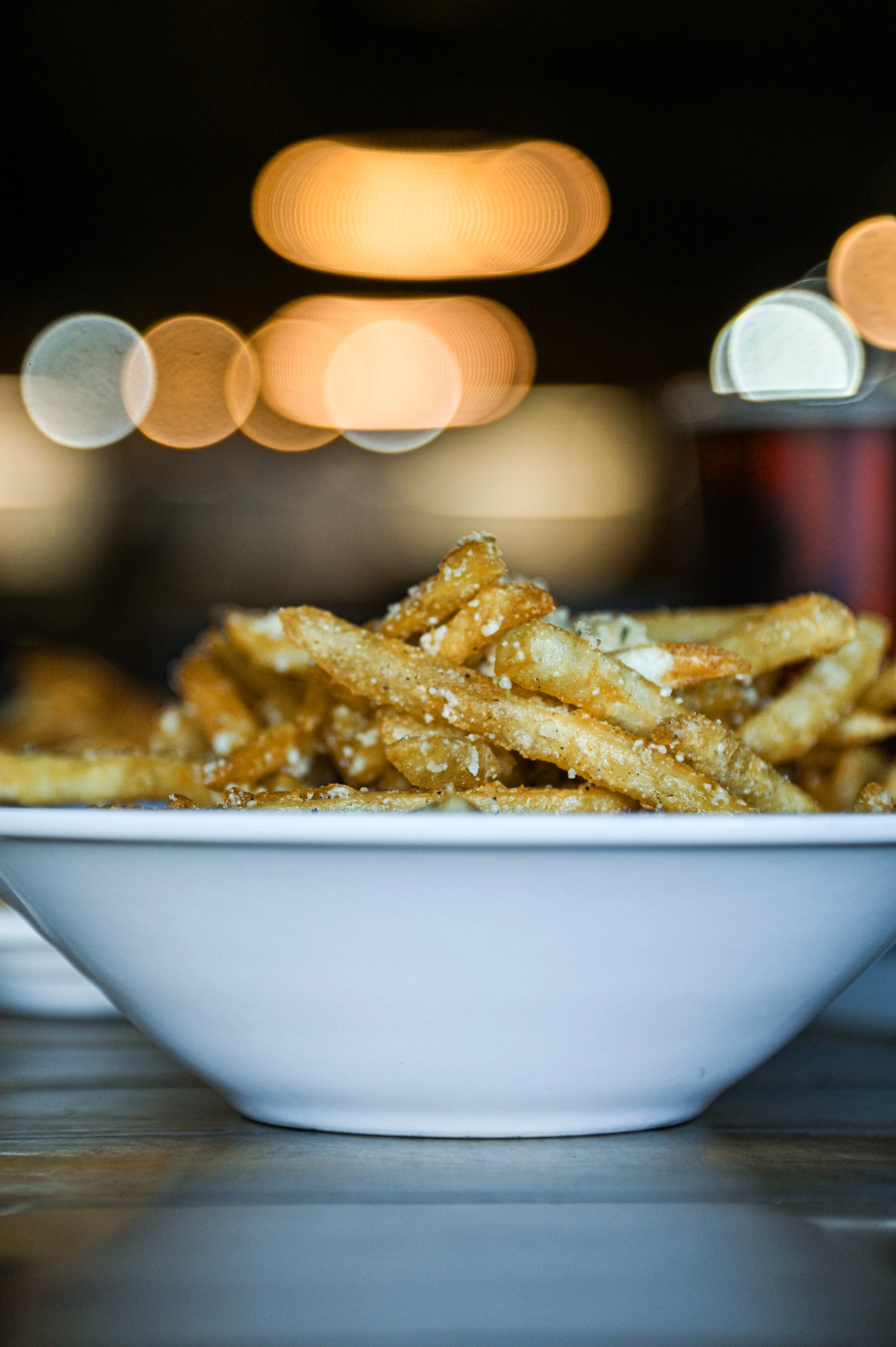 Close-up of a bowl of French fries with melted cheese on top, and bokeh lights in the background.