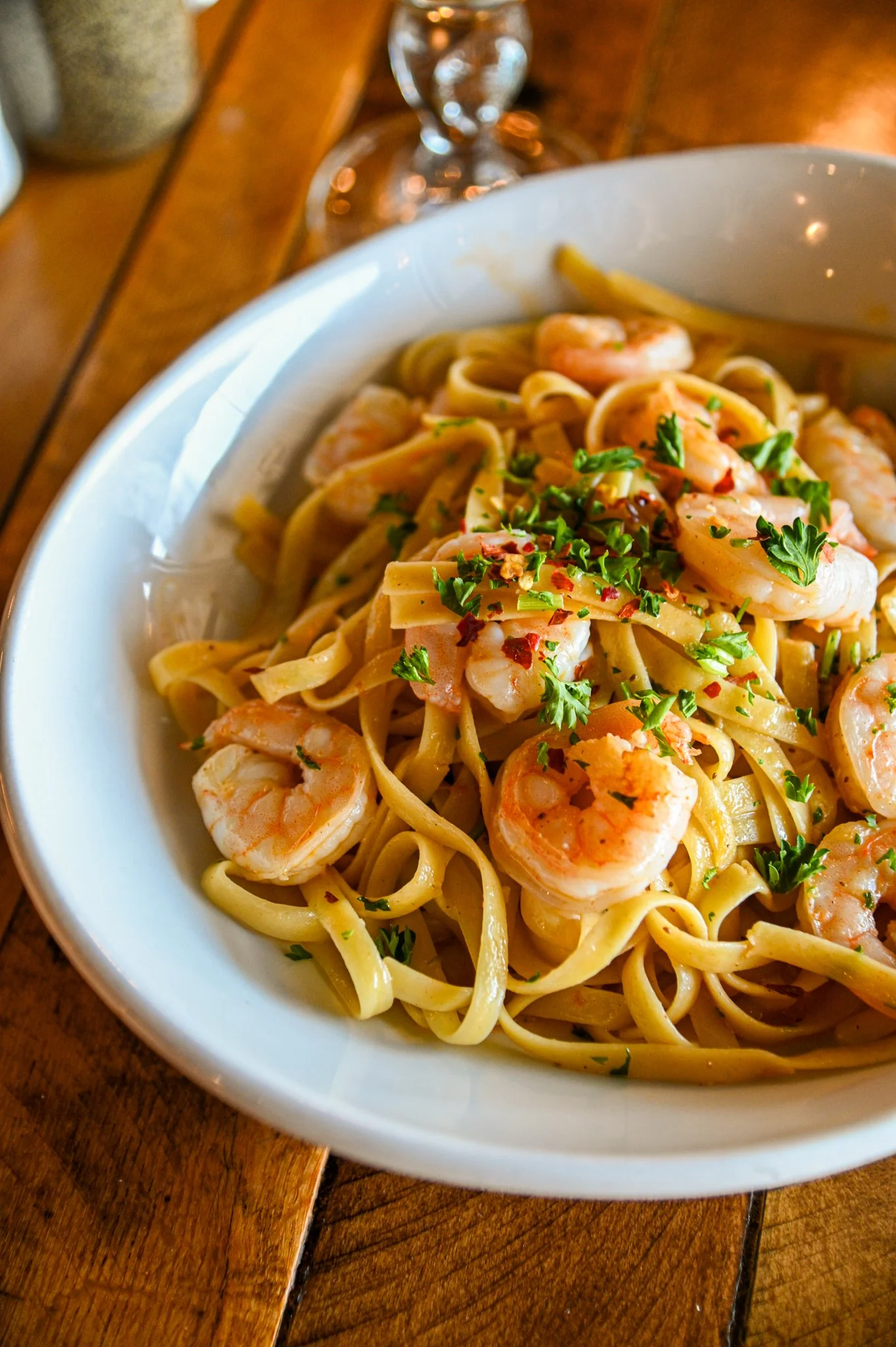A bowl of shrimp pasta garnished with chopped parsley and red pepper flakes on a wooden table.