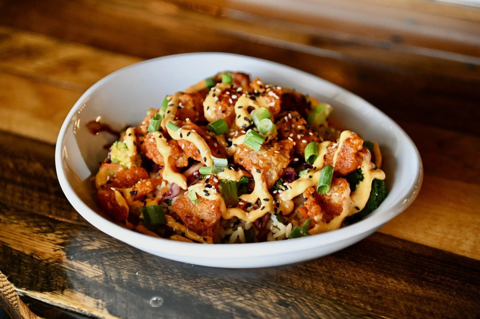 A bowl of Asian-inspired spicy salmon and rice dish garnished with green onions and sesame seeds, drizzled with sauce.