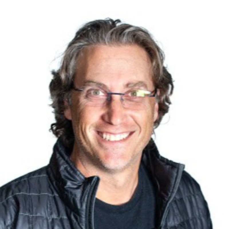 A smiling man with glasses and wavy gray hair wearing a black jacket against a plain white background.