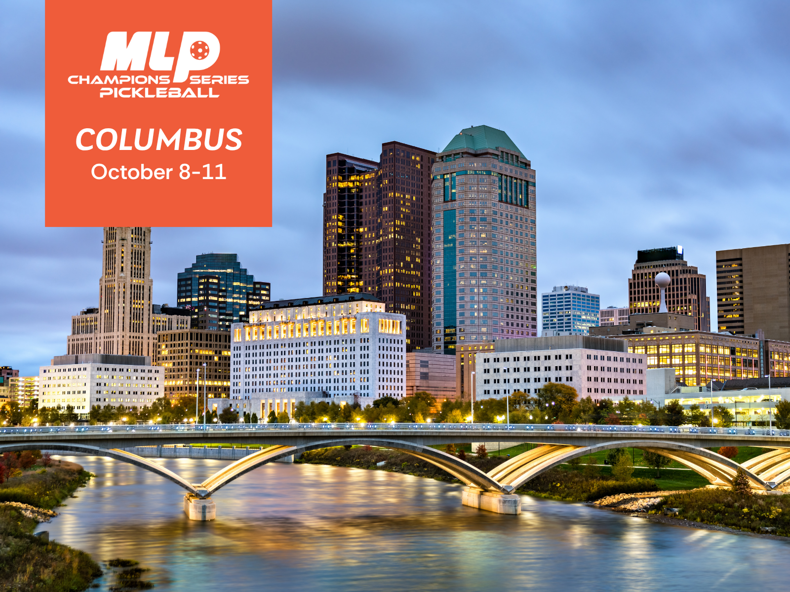 Nighttime view of the Columbus, Ohio skyline with tall buildings, a bridge over a river, and a cloudy sky.