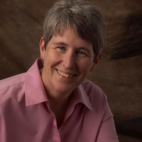 A woman with short gray hair wearing a pink shirt, smiling at the camera.