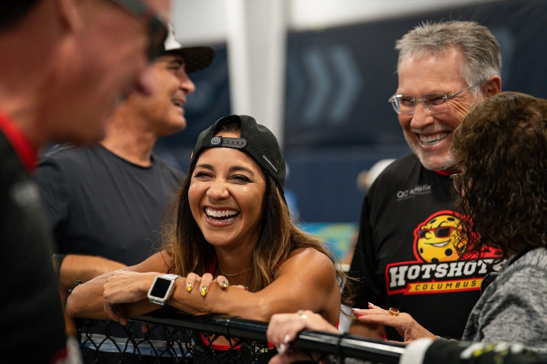 Group of people smiling and laughing at an event, with some wearing TeamHotshot Columbus shirts and caps.