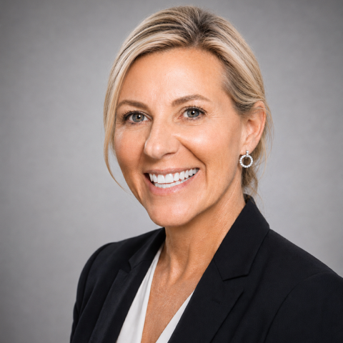 Professional woman with blonde hair, smiling, wearing a black blazer and white top, against a gray background.