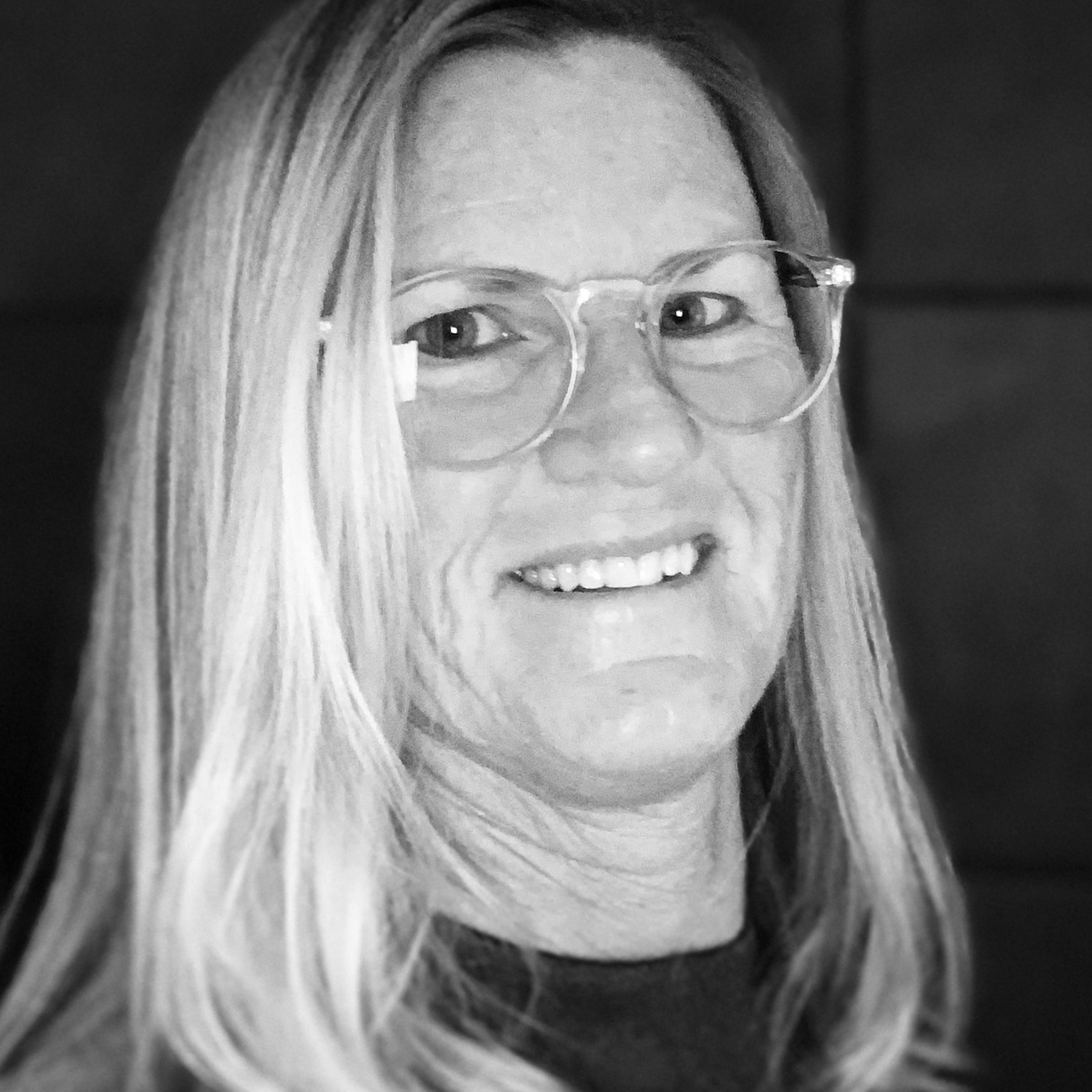 Close-up black-and-white photo of a smiling woman with long hair wearing large round glasses.