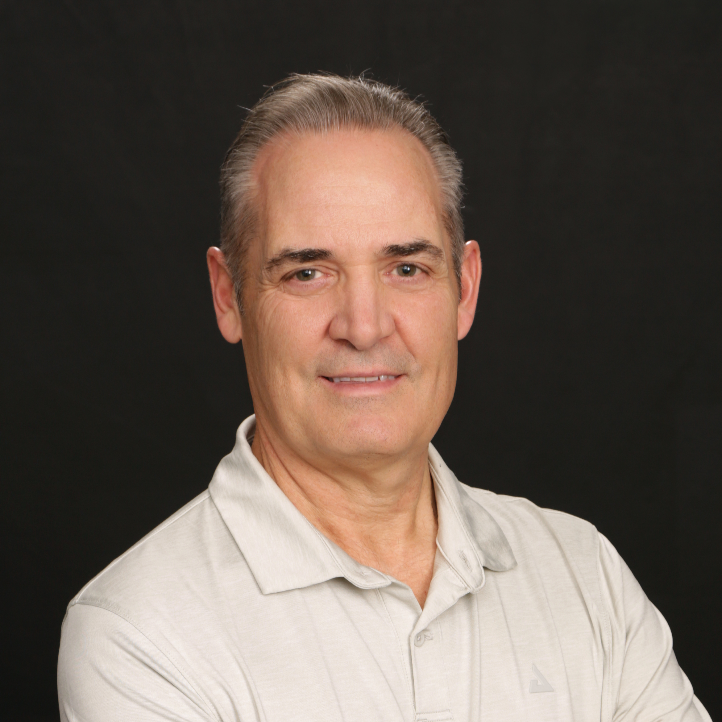 Close-up of a man's face with gray hair, green eyes, smiling, wearing a light gray collared shirt against a black background.