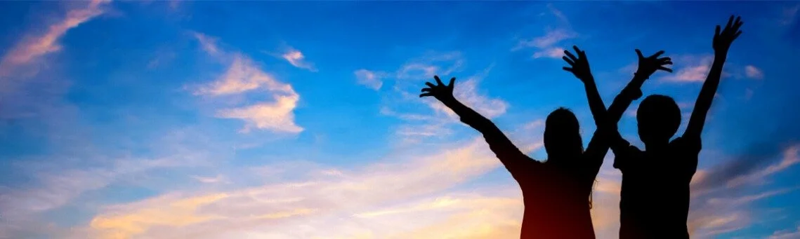 Silhouette of two children with arms raised against a sunset sky with clouds.