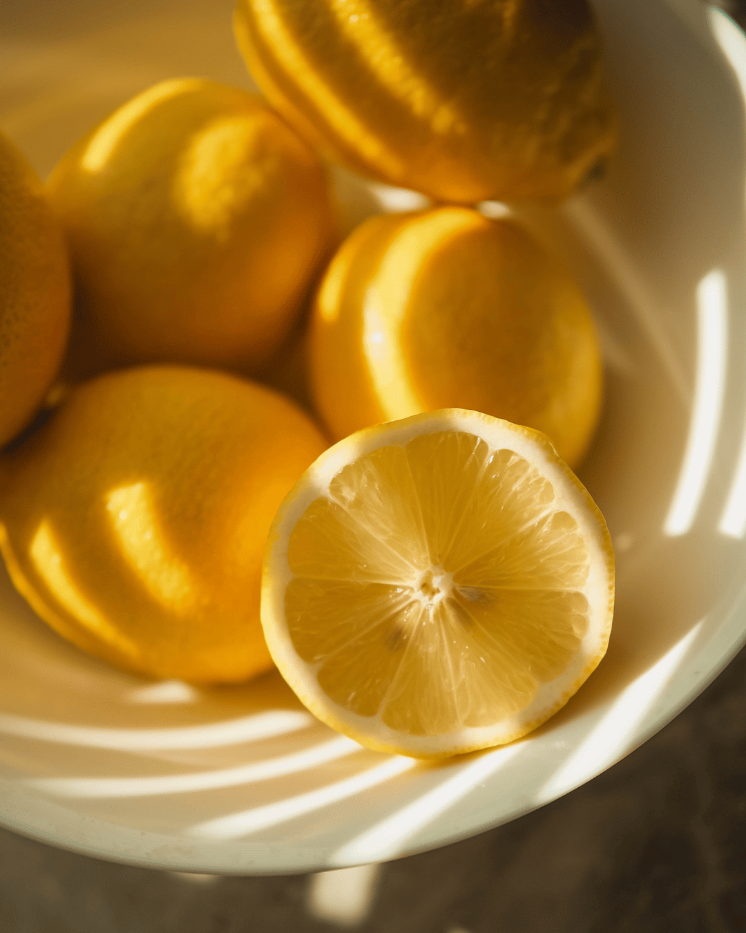 Lemon with some whole lemons in a white bowl.