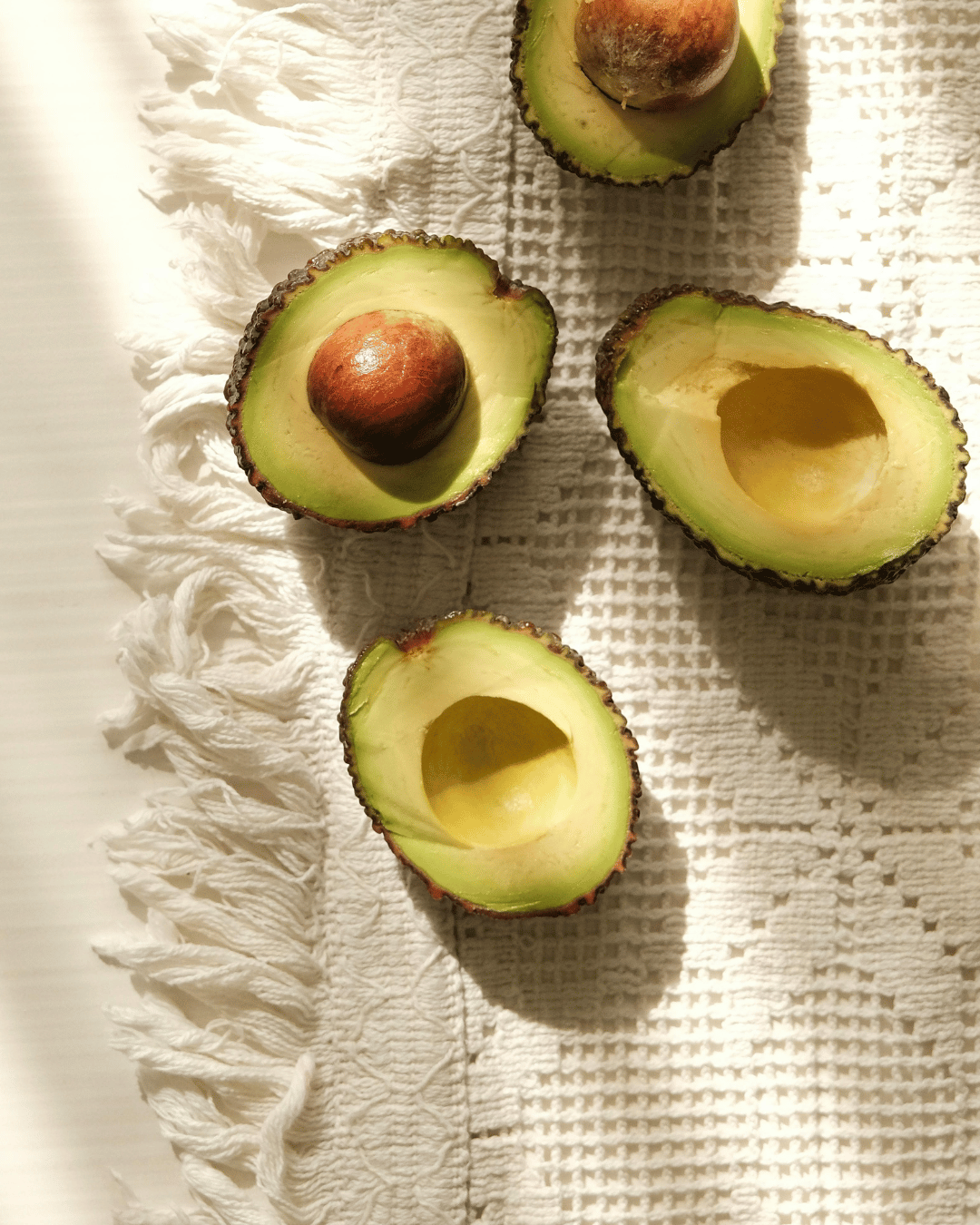 Halved avocados with pit inside on white textured cloth.