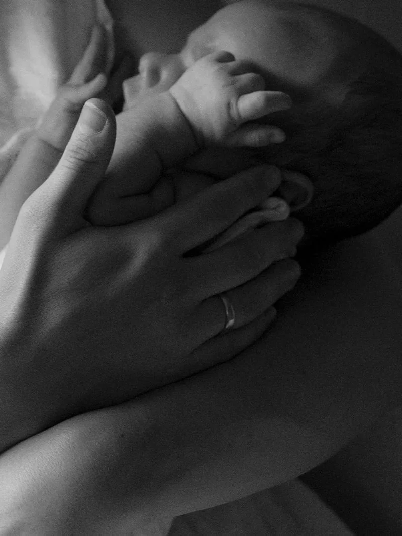 Close-up of a person holding a baby's hand, with the baby lying on their shoulder, in black and white.