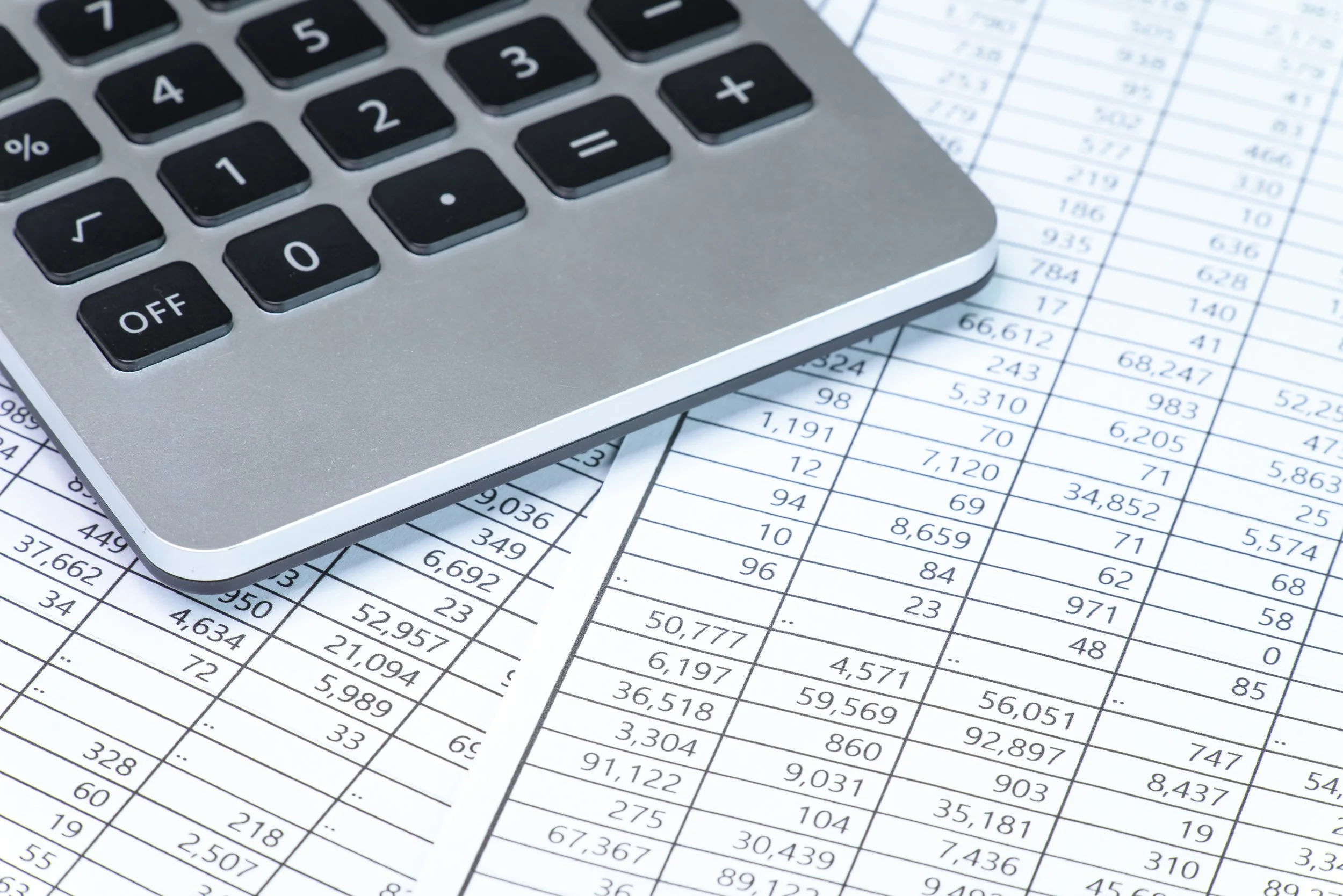 A close-up of a calculator placed on top of printed spreadsheets with numerical data.