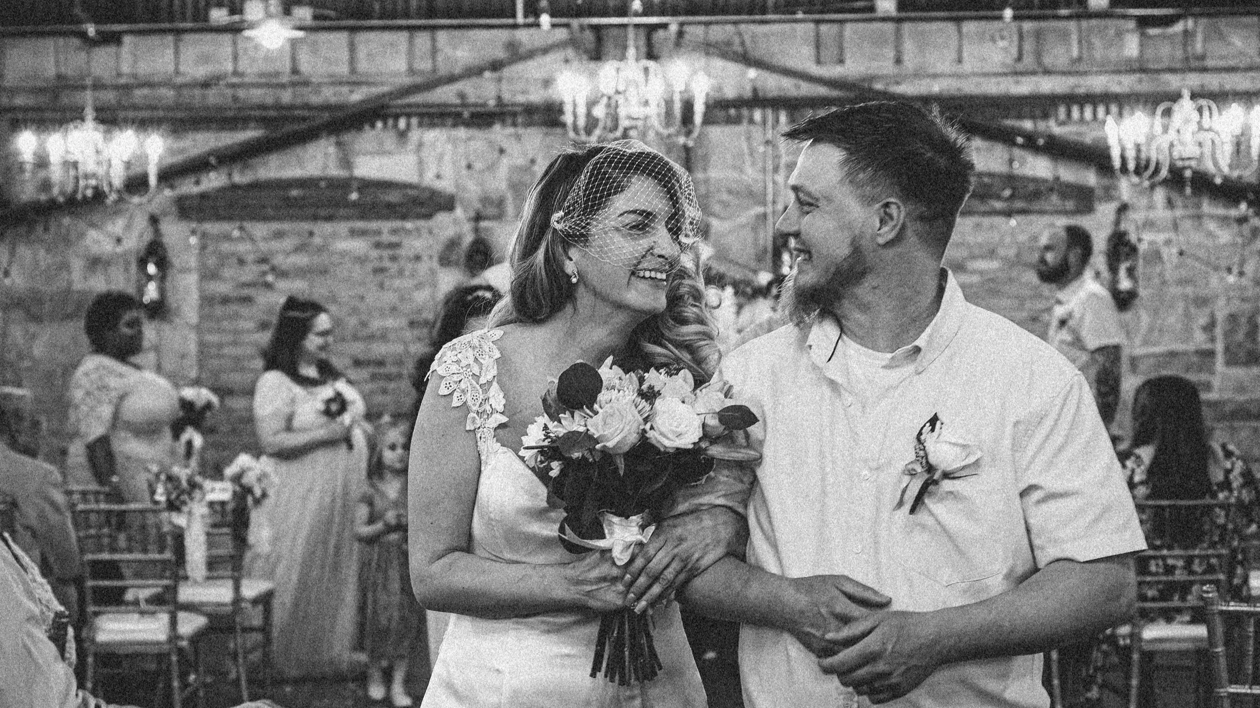 Black and white candid photo of a bride and groom smiling closely at their wedding reception, captured in Snap Sync Studio's documentary style.