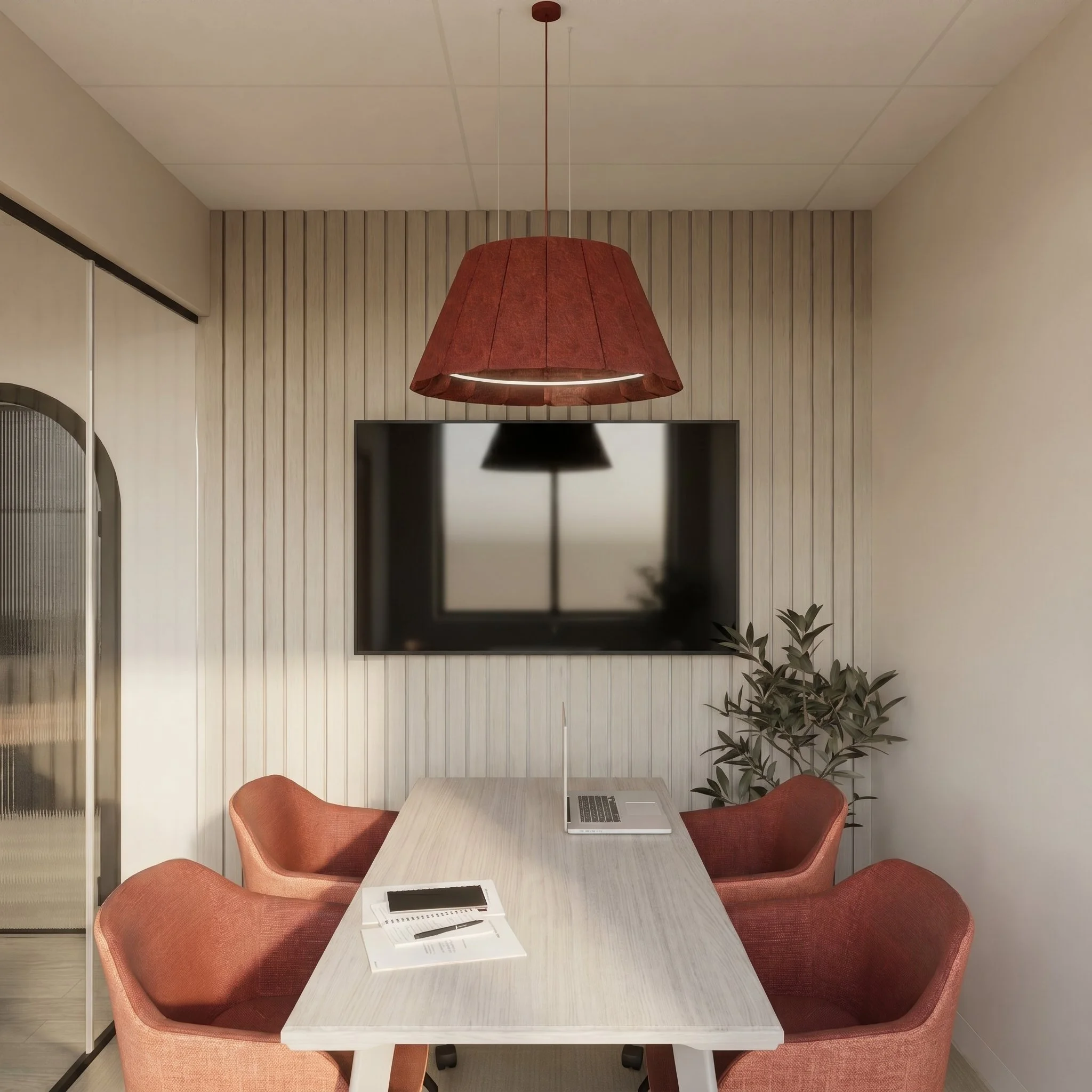 Salle de réunion avec une table en bois clair, quatre chaises en tissu rouge, un ordinateur portable, et des documents. Mur en bois clair derrière avec téléviseur et plante verte à droite.
