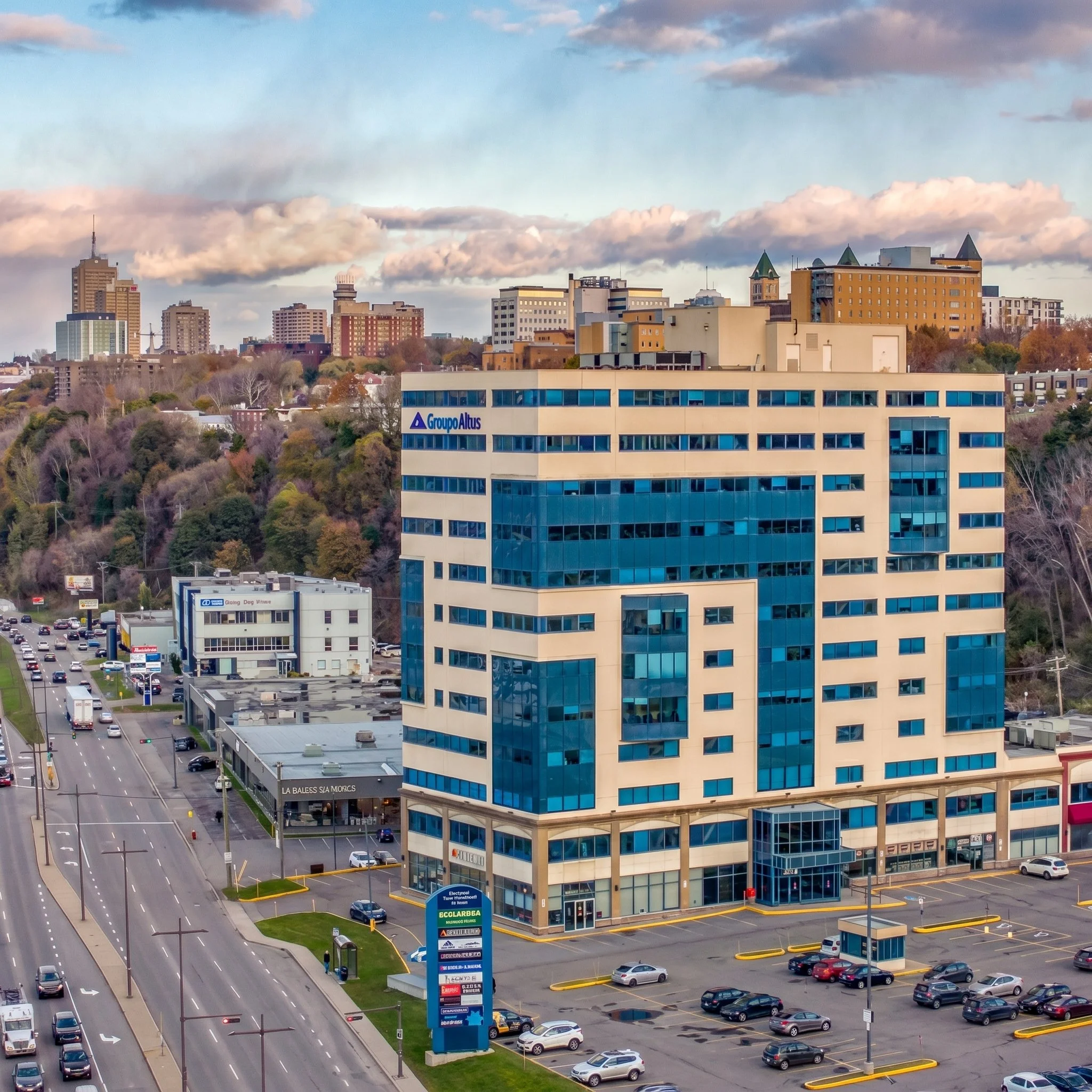 Vue d'une ville avec des immeubles modernes, une route avec des voitures et un parking, des panneaux publicitaires, le ciel avec des nuages et des bâtiments en arrière-plan. Immeuble qui appartient à la famille Groleau