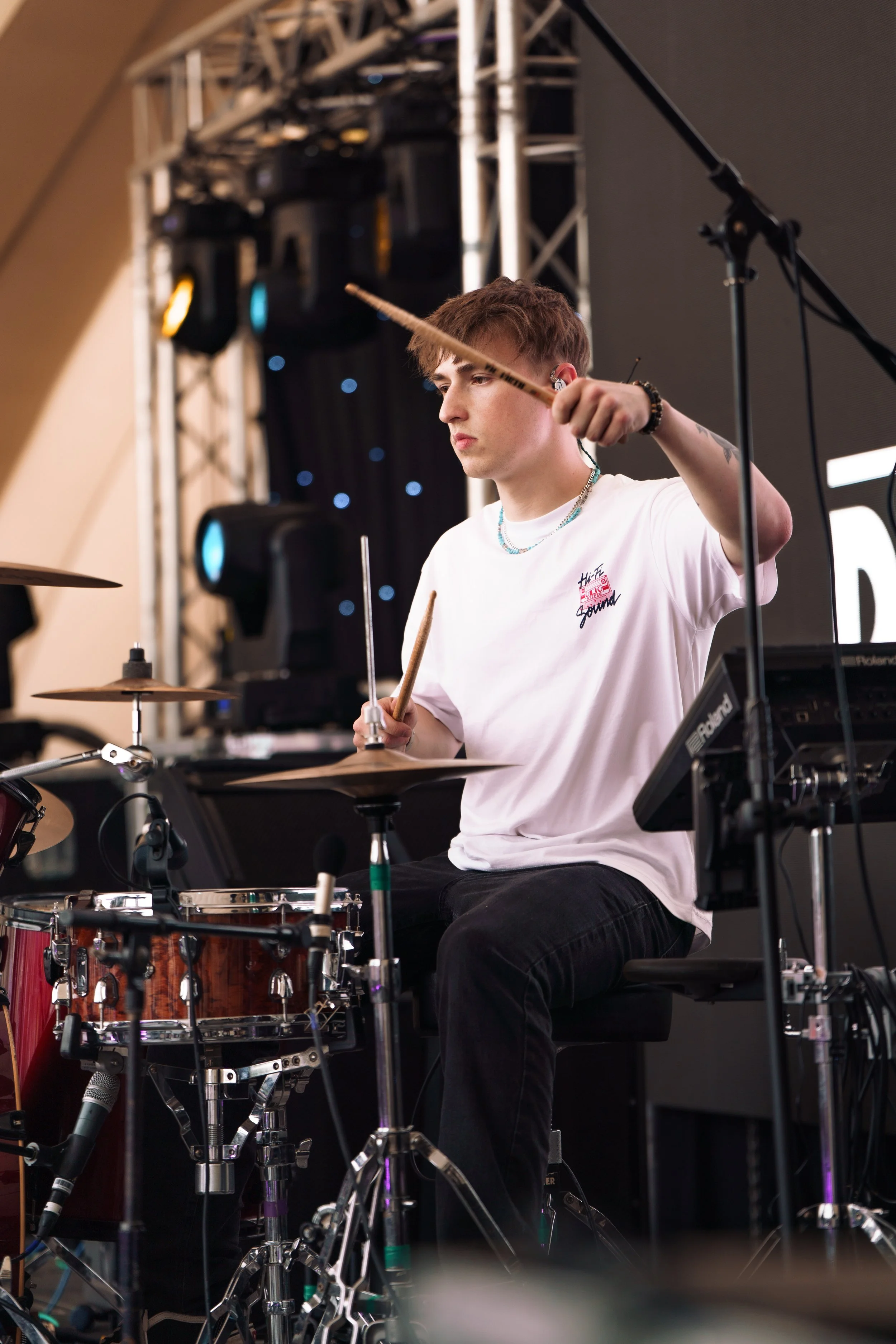 Young man playing drums on stage with stage lights and equipment in the background.