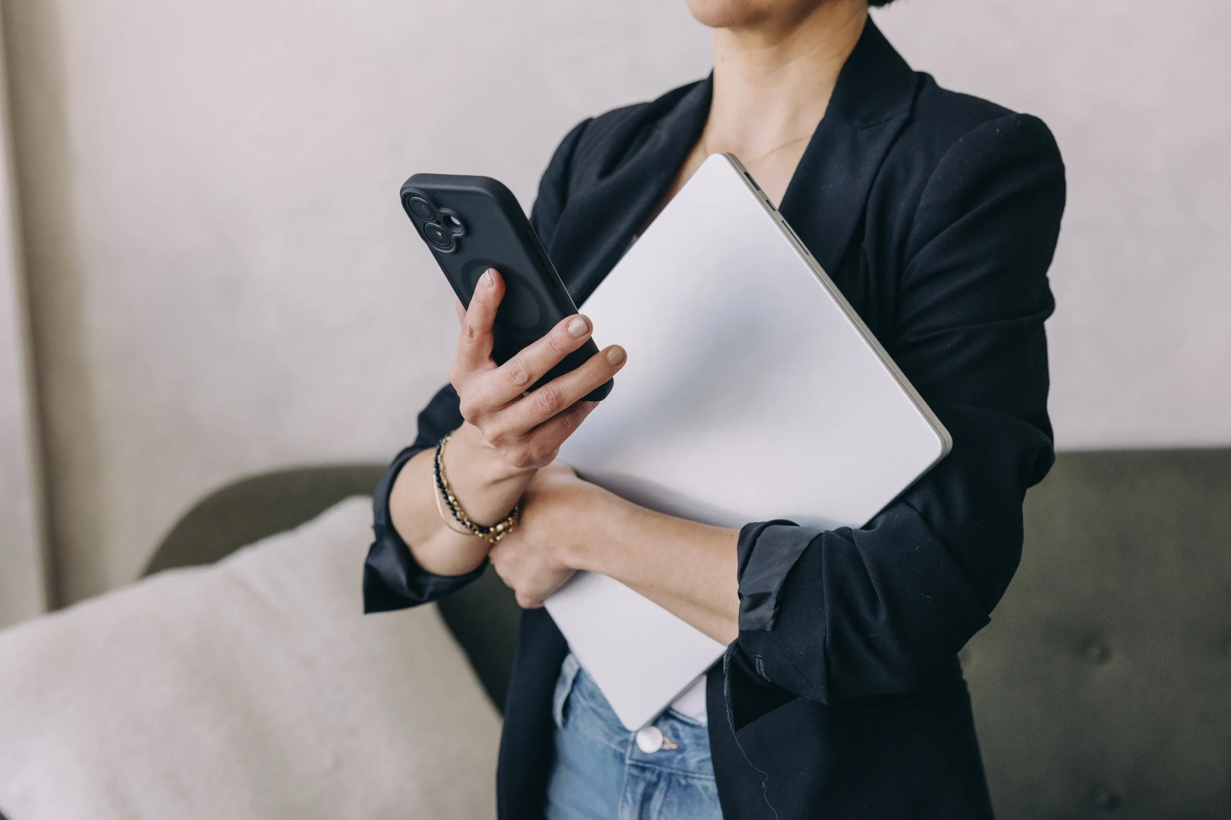 Woman in a blazer holding a phone and laptop, representing hands-on execution support.