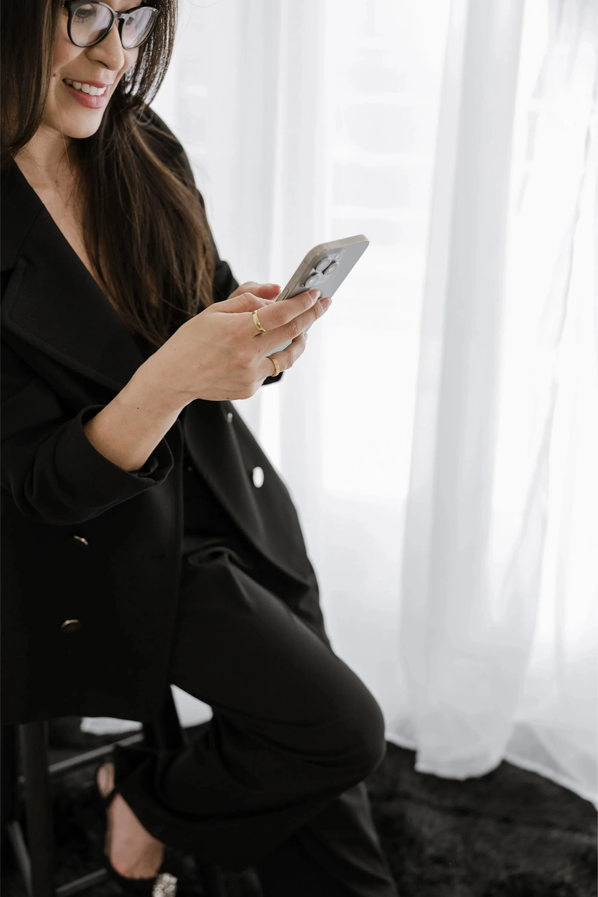 Woman in a black blazer smiling at her phone, representing confident, composed leadership.