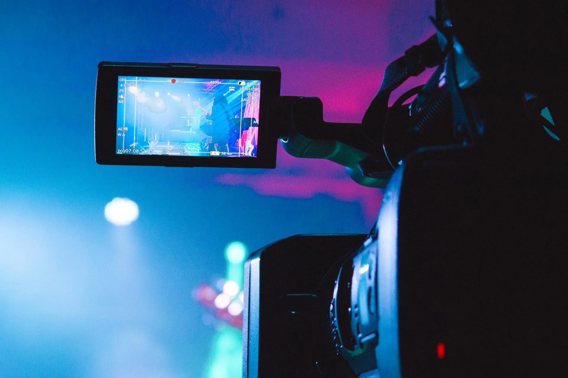Close-up of a video camera recording a colorful stage with blue and purple lighting, seen through the camera’s display screen.
