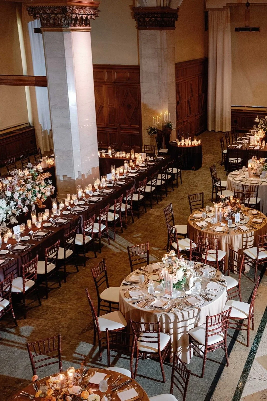 Elegant banquet hall wedding reception decorated with round and rectangular tables set for a formal event, featuring floral centerpieces, candles, and gold and white tableware.