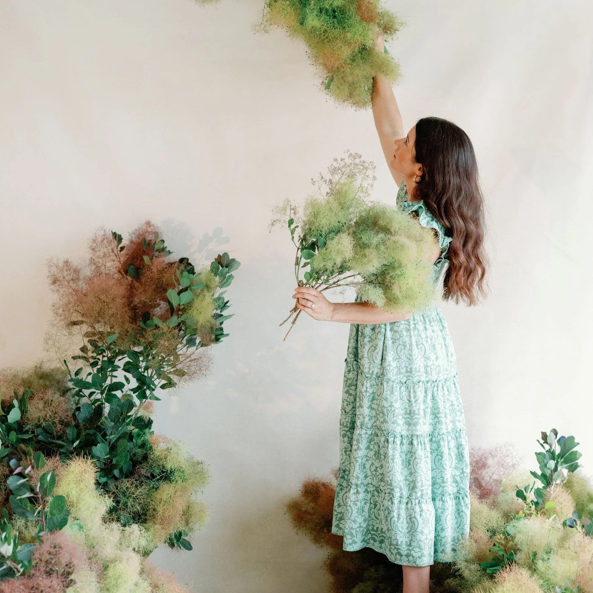 Lead wedding planner installing smoke brush and greenery floral installation against creamy neutral backdrop