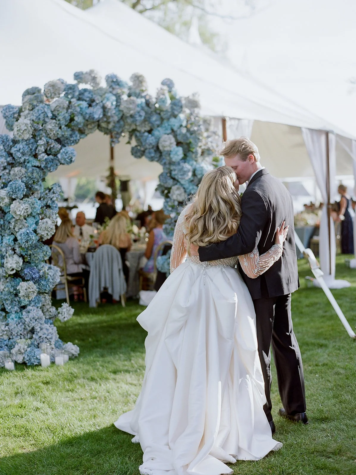 Bride and groom stealing a kiss in front of a chic blue and white hydrangea arch leading into their wedding reception