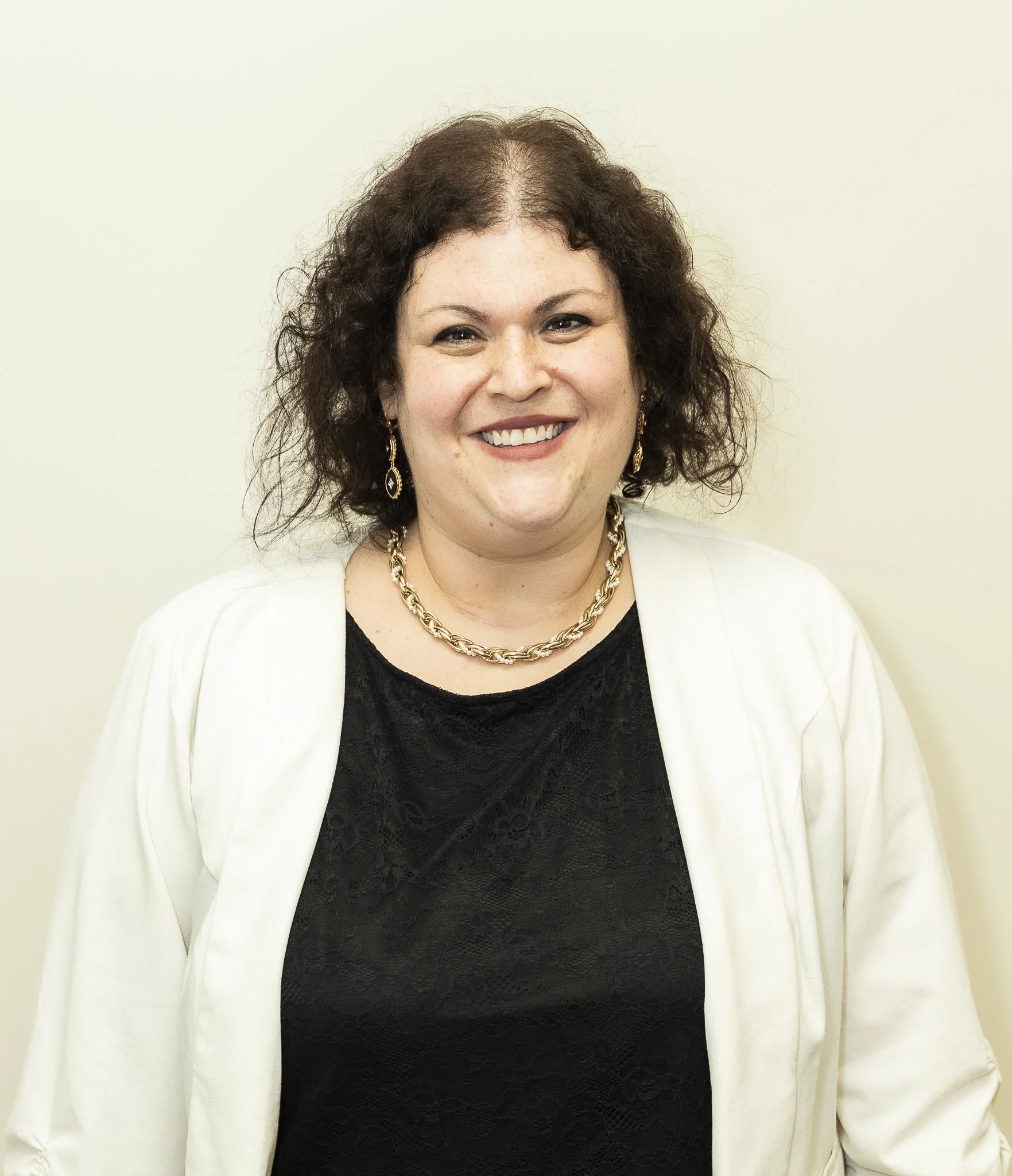 Professional headshot of a smiling small business owner wearing a black top and white cardigan, facing the camera against a neutral background.