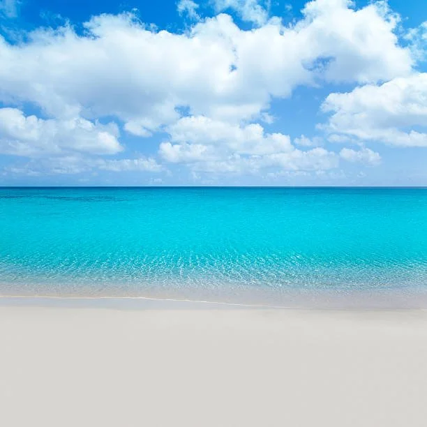 Empty sandy beach with turquoise ocean and blue sky with scattered clouds