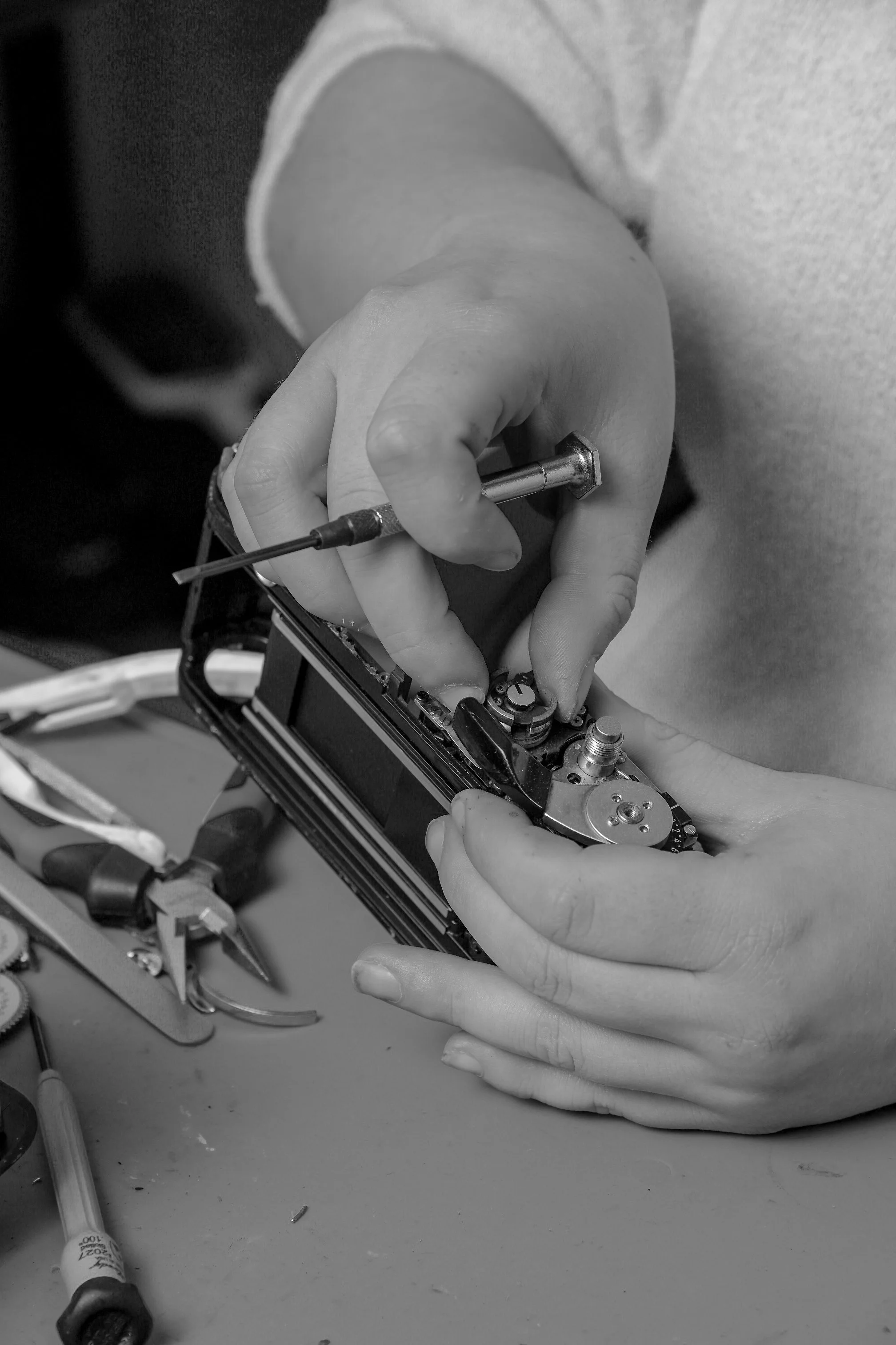 Close-up of a person using a precision screwdriver to work on electronic device or small machinery, with various tools on a work surface.