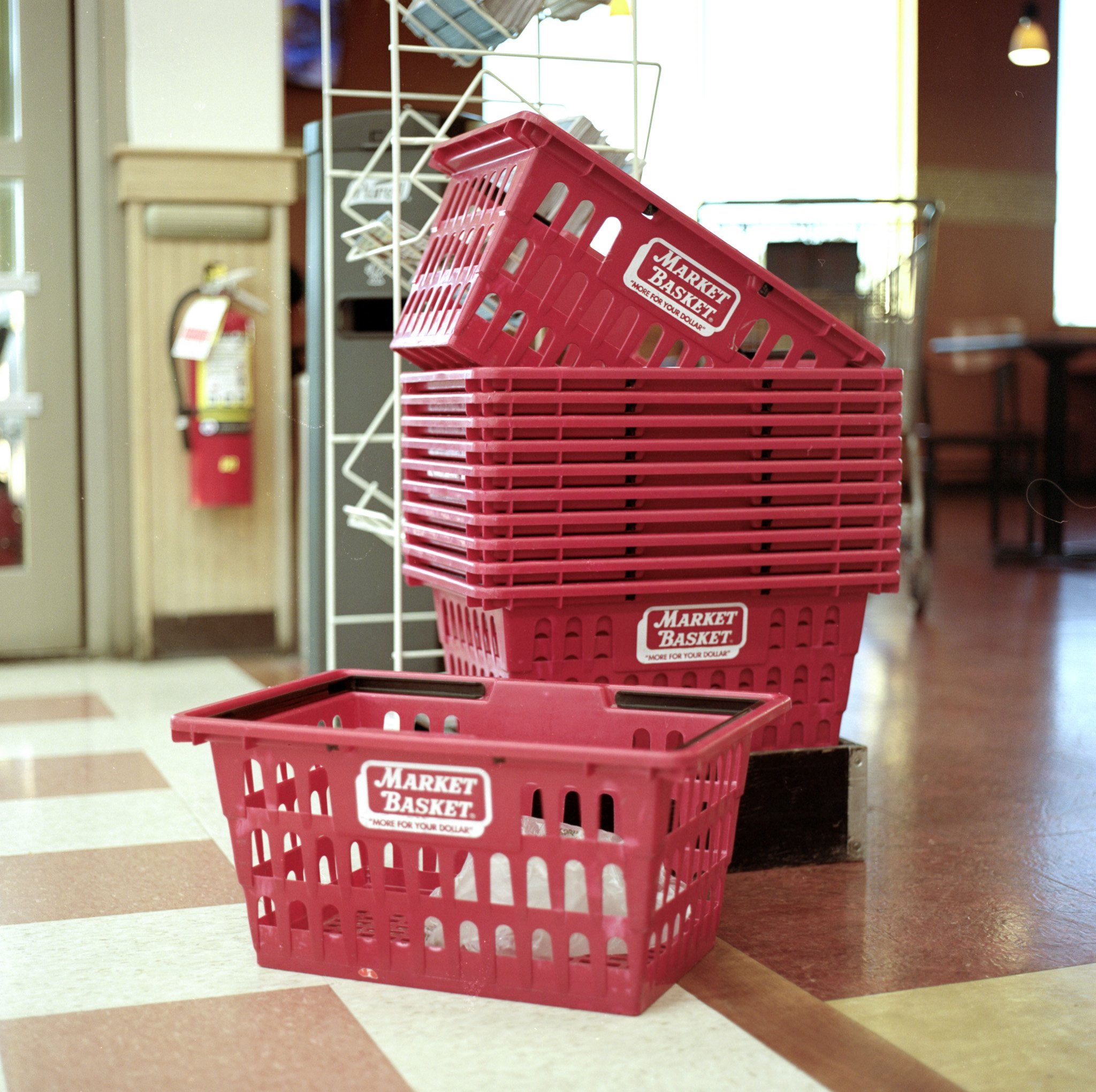 Red shopping baskets stacked together on the floor of a grocery store or retail location.