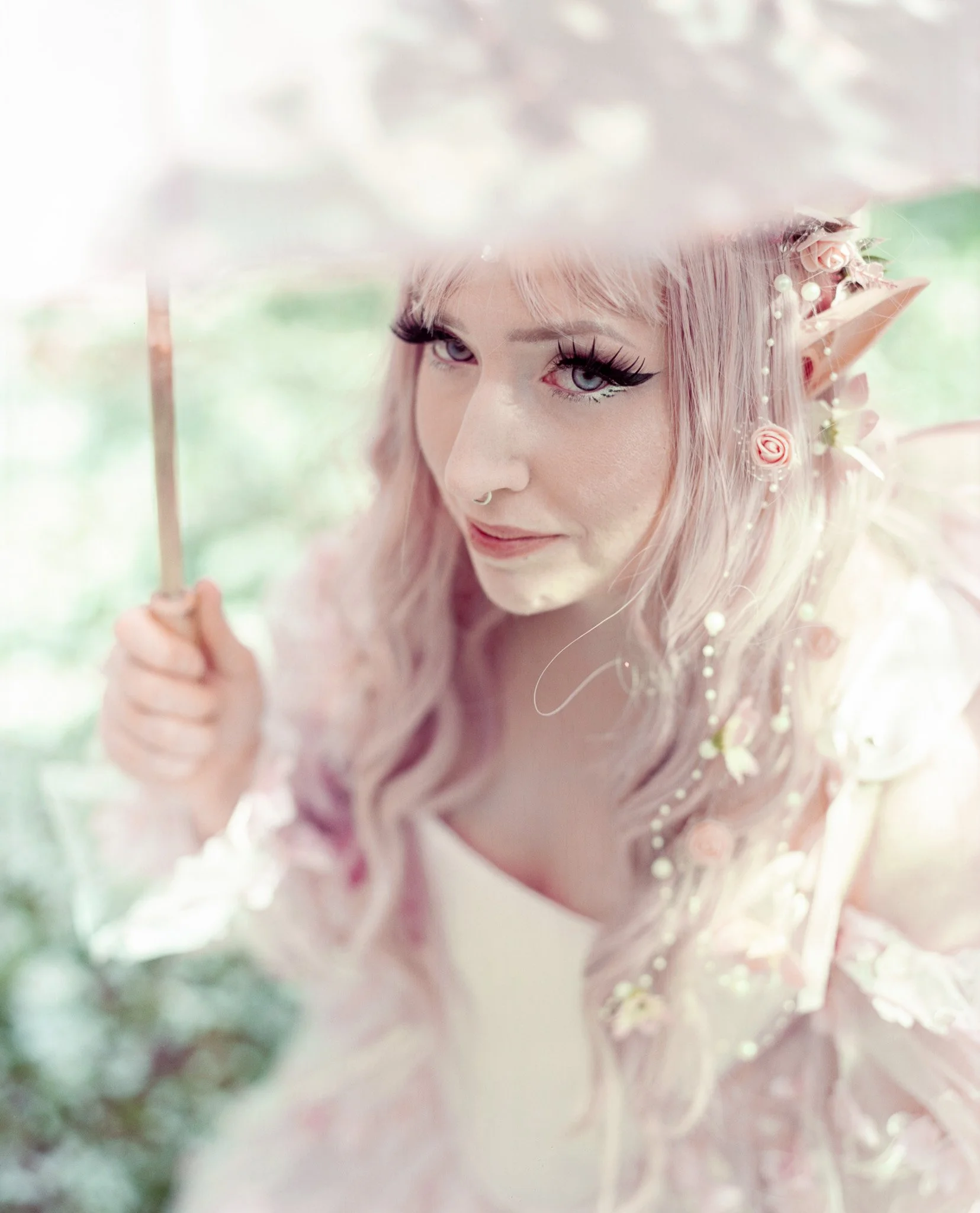 A woman with elf-like features, pink hair, large violet eyes, and pointed ears, holding a parasol, wearing a pink floral outfit.