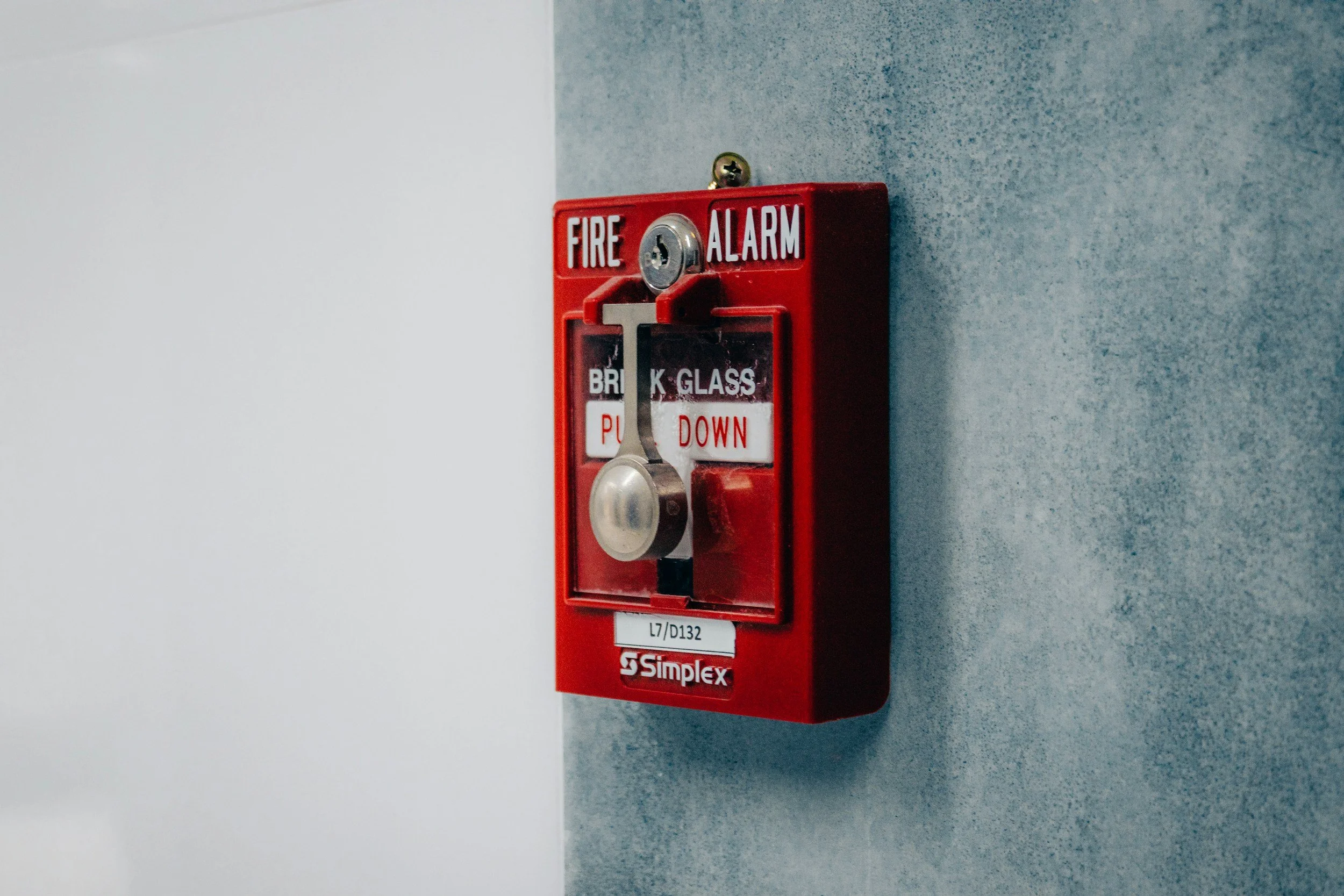 Red fire alarm with a pull chain and warning label, mounted on a gray wall.