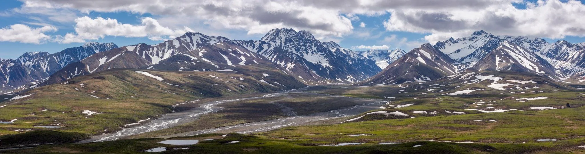 Panoramic view of snow-capped mountains with green valleys and a river flowing through the landscape.
