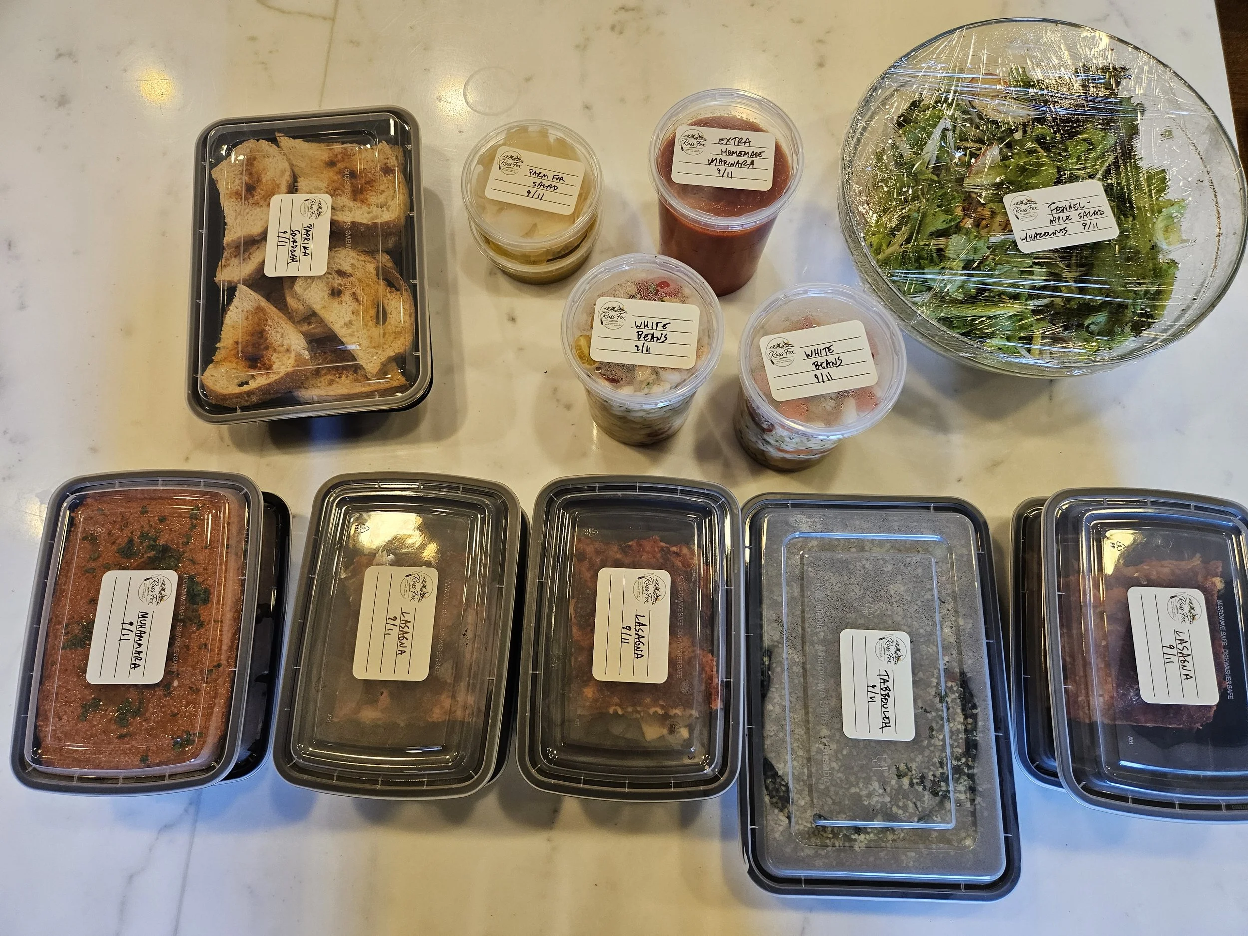 Labeled meal-prep containers with prepared meals, sides, and salad.