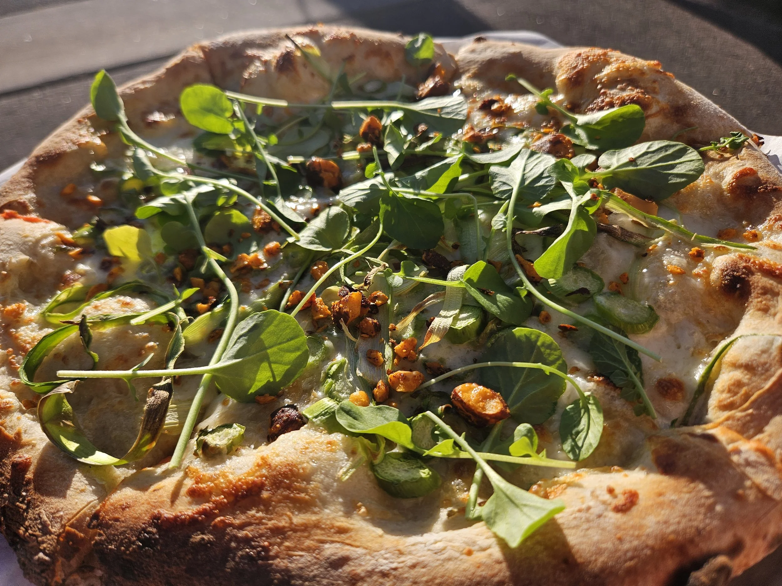 Close-up of a pizza with cheese, arugula, and roasted garlic on a wooden table.