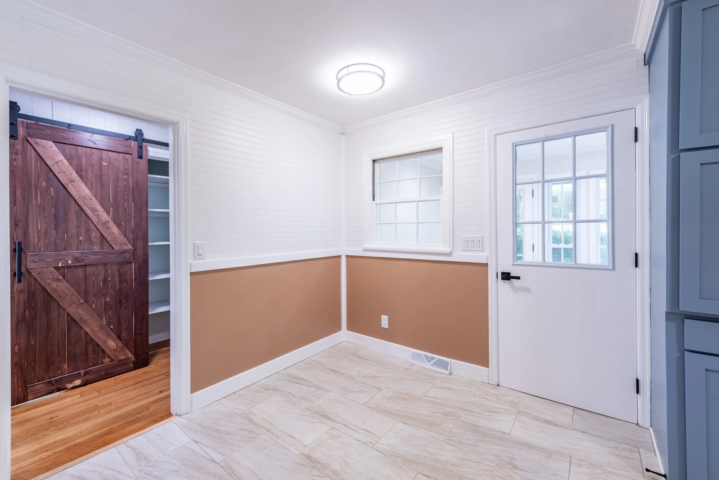 Entryway with white and peach walls, beige tiled floor, a wooden sliding barn door, and two windows letting in natural light.