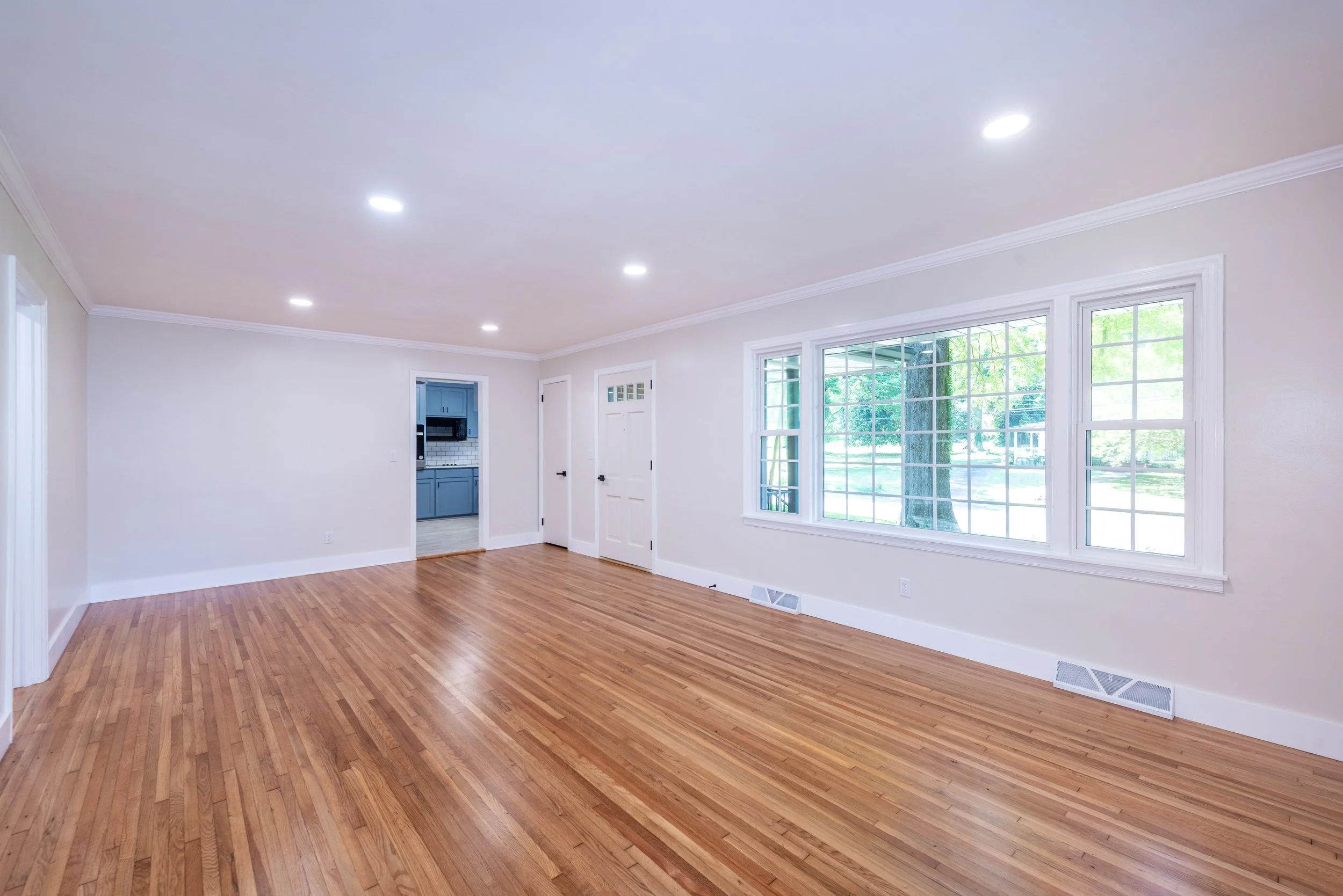 Empty living room with hardwood floors, large windows, and white walls.