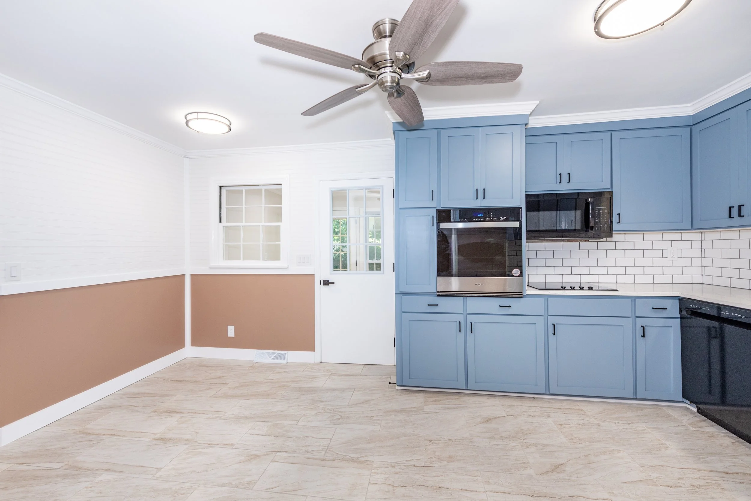 Kitchen with blue cabinets, white subway tile backsplash, ceiling fan, and wood-look tile flooring.