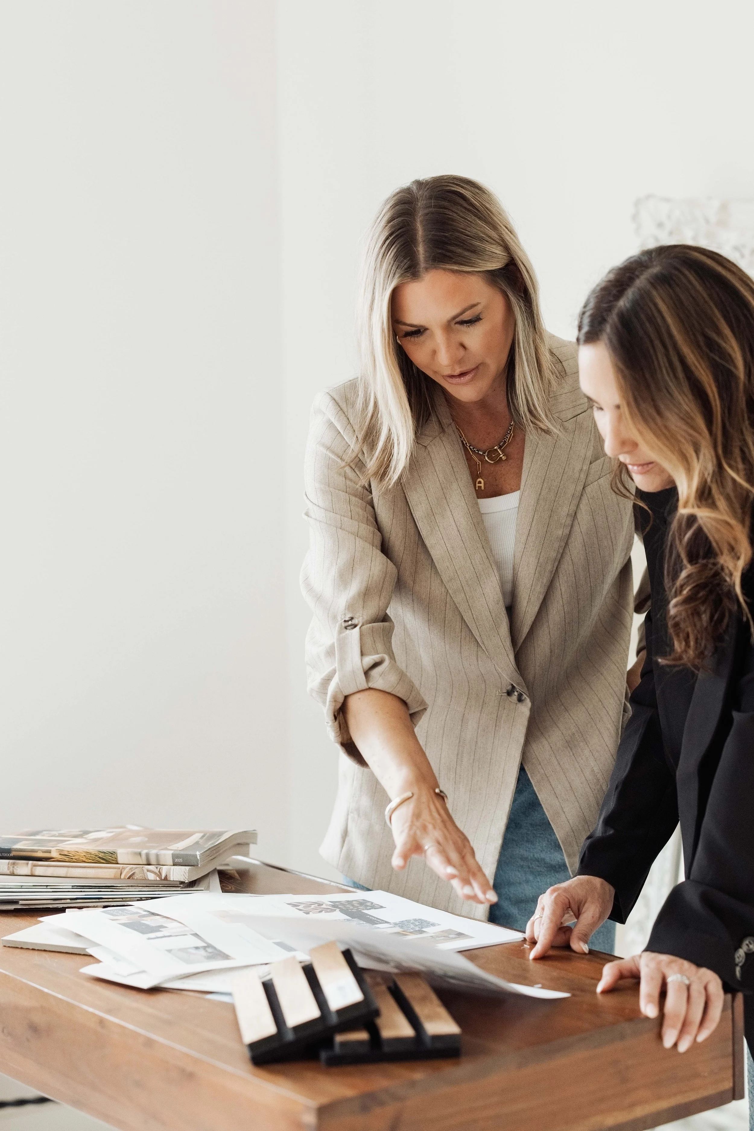Ashley Walkley discussing and reviewing printed materials on a wooden table, with design samples and color swatches spread out in an office or studio setting.