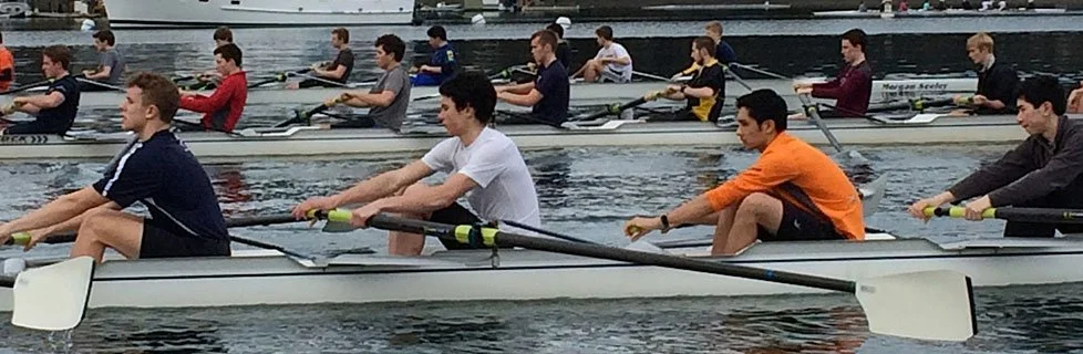 Group of young men rowing racing shells on a body of water.