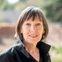 A woman with shoulder-length brown hair and a black shirt, smiling outdoors.
