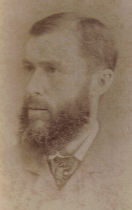 A sepia-toned portrait of a Timothy Byron Rider with a full beard and mustache, wearing a collared shirt and tie.