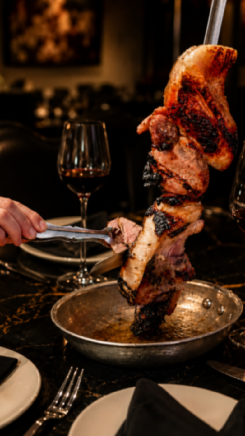 Server carving Brazilian-style grilled meat tableside over a black-and-gold epoxy table at Melting Borders Kitchen & Sips.
